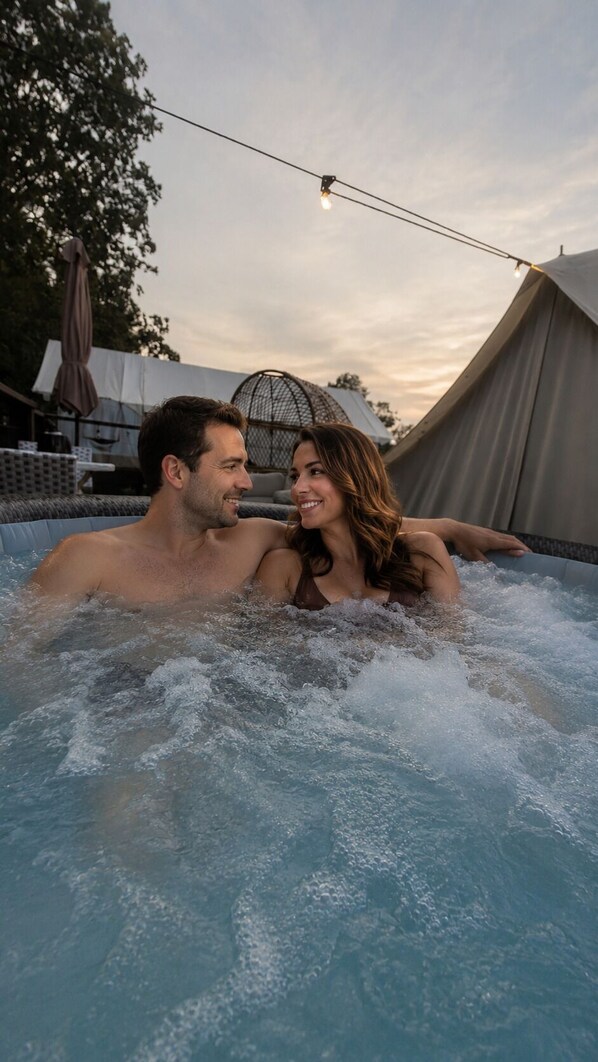 A couple in a hot tub with a tent and outdoor furniture in the background.
