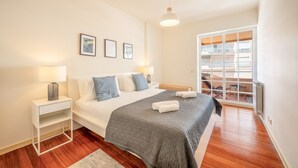 Un dormitorio moderno con cama, mesitas de noche, un ventanal y vistas al balcón exterior.
