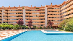 Un hotel de varios pisos con piscina central, rodeado por un patio con árboles y un camino empedrado.