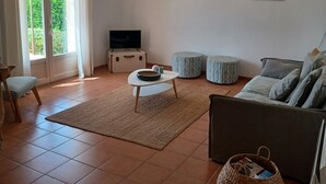 A living room with a sofa, a coffee table, a TV, and a large window with curtains.