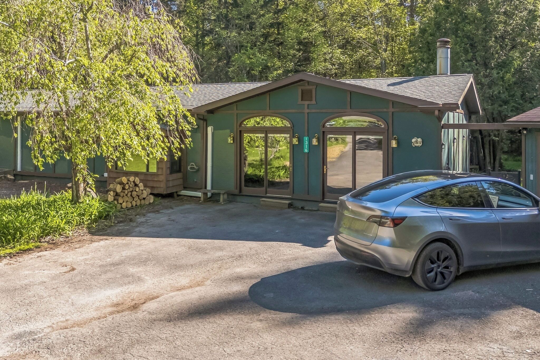 Un bâtiment à l’extérieur verdoyant, avec deux portes et une voiture garée devant.
