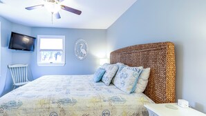 A bedroom with a bed, a television, a window, and a ceiling fan.