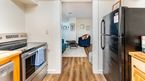 Et køkken med komfur, ovn og køleskab, der giver adgang til et opholdsområde med sofa og sofabord.
