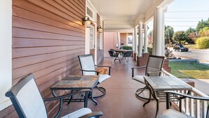 En overdækket veranda med udendørs siddepladser, en murstensvæg og udsigt til en gade.