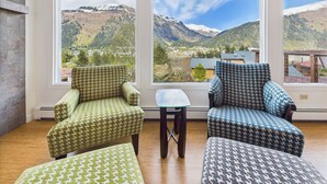 A room with large windows offering a mountain view, a small table, and two patterned armchairs. - Admiral’s View | Panoramic Views, Family Friendly (Juneau)