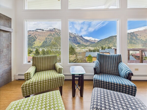 A room with large windows offering a mountain view, a small table, and two patterned armchairs. - Admiral’s View | Panoramic Views, Family Friendly (Juneau)