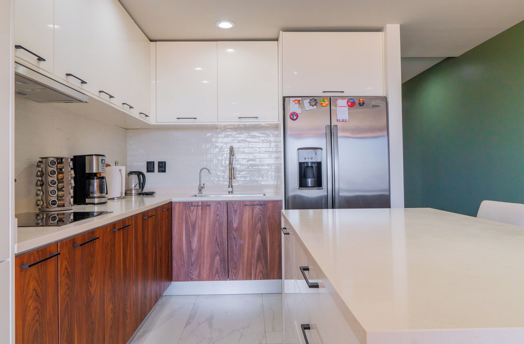 A modern kitchen with white cabinets, a wooden countertop, a stainless steel refrigerator, and a coffee maker.