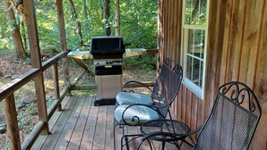 A covered wooden deck with a grill, metal chairs, and a table. -  Cozy Off Grid Cabin near the Blueridge Parkway and Appalachian Trail. (Monroe)