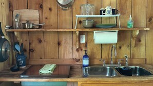 A wooden kitchen with a sink, a shelf with glassware, and a trash bin. -  Cozy Off Grid Cabin near the Blueridge Parkway and Appalachian Trail. (Monroe)