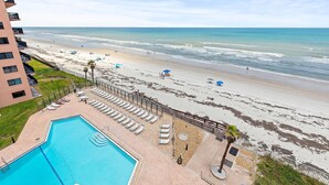 Ein Hotel direkt am Strand mit Swimmingpool, Sonnenschirmen und Liegestühlen.