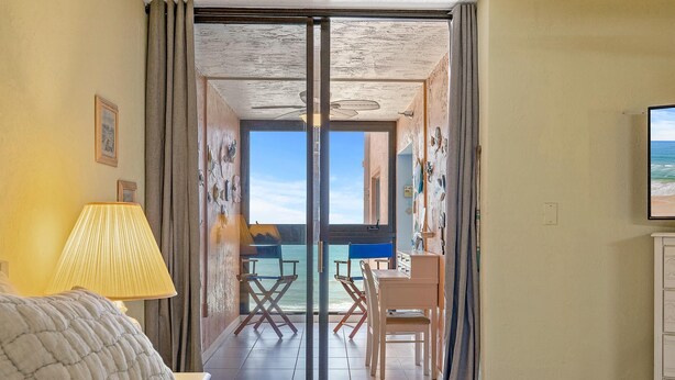 Ein Hotelzimmer mit einem Bett, einem Schreibtisch und Meerblick durch eine Glastür.