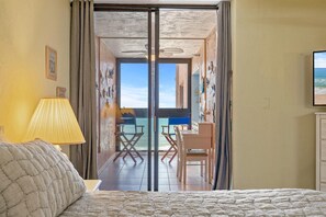 A hotel room with a bed, a desk, and a view of the ocean through a glass door. - Sunrise 602 (New Smyrna Beach)