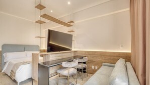 Ein modernes Hotelzimmer mit Bett, Sofa, Schreibtisch mit Stuhl und Wand-Fernseher.
