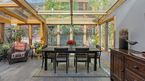Ein Wintergarten mit Glasdecke, Holzbalken, einem Esstisch mit Stühlen und Topfpflanzen.