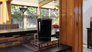 Eine Kaffeemaschine auf einem Tablett in einer Küche mit einer Holz Arbeitsplatte, einem Fenster mit Blick auf Grünflächen und einer Pendelleuchte.