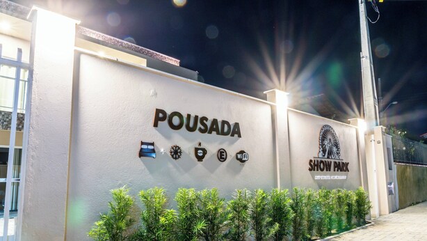 Un mur sur lequel on peut lire l’inscription « POUSADA SHOW PARK » ainsi que des symboles indiquant la présence du Wi-Fi, d’un parking et d’autres commodités.