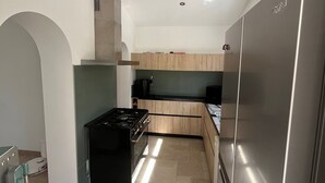 Eine moderne Küche mit Edelstahlkühlschrank, Gasherd, Holzschränken und Fliesenboden.