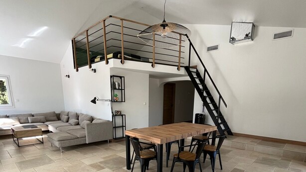 Ein geräumiger Wohnbereich mit großem Holzesstisch und Stühlen, einer eingebauten Couch und einer Treppe, die zu einer oberen Ebene führt.