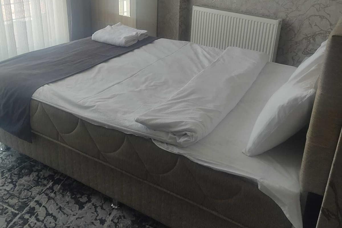 A neatly made bed with white linens, a grey headboard, and a marble-patterned floor.