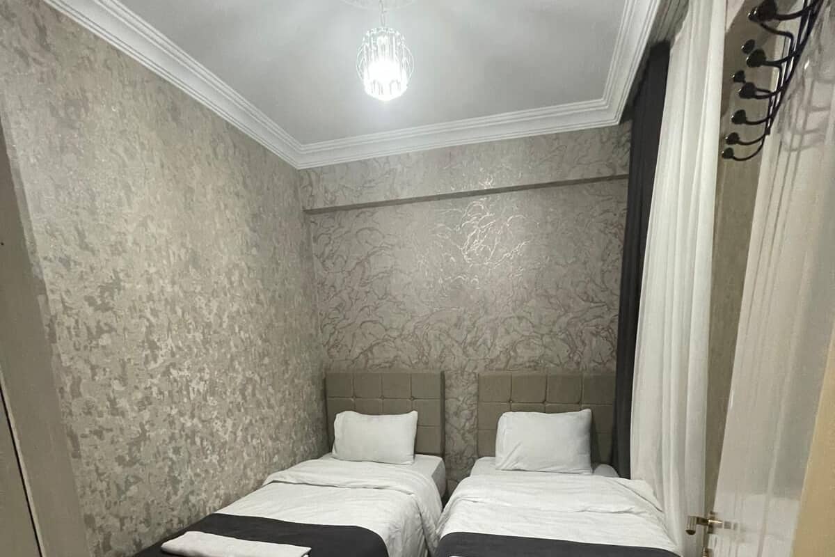 A room with two beds, a chandelier, a patterned floor, and a door with a coat rack.