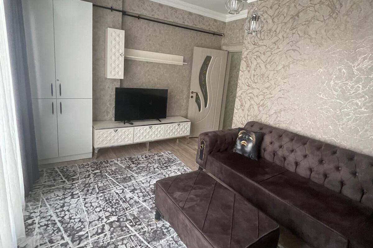 A modern living room with a dark brown sofa, a flat-screen TV, and a patterned rug.