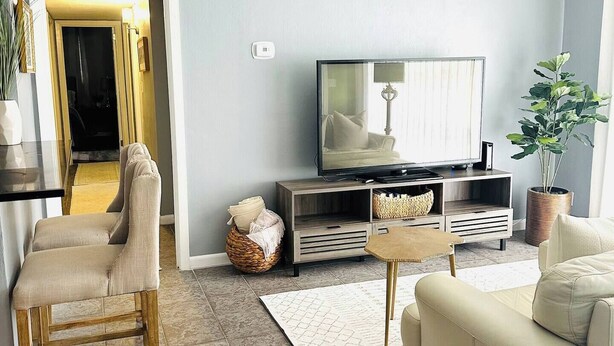 Ein Wohnzimmer mit Fernseher, Sofa und Sesseln. Eine Tür führt in einen anderen Raum.