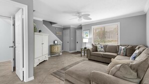 A spacious living room with a beige sofa set, a white cabinet, and a ceiling fan.
