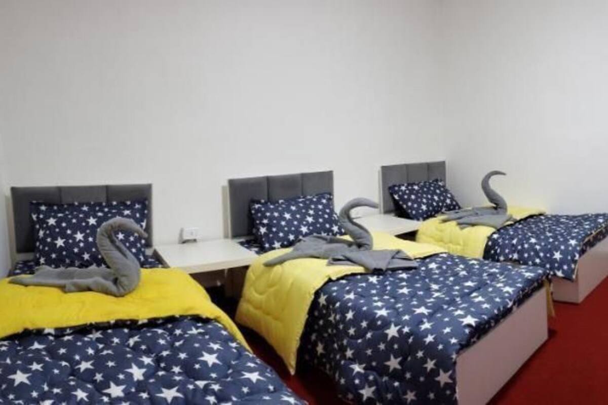 A hotel room with three beds, each with a star-patterned bedspread, a small table, and a red carpet.