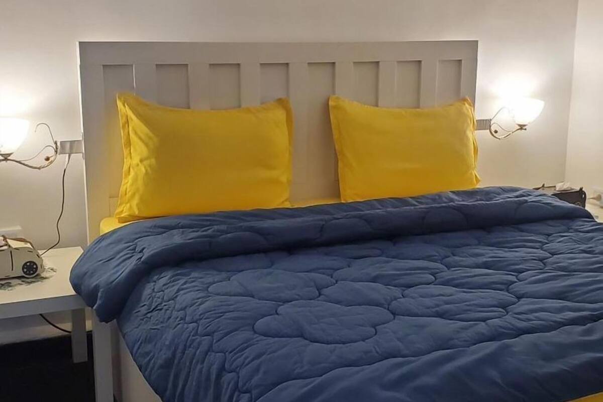 A bed with a white headboard, two yellow pillows, and a blue blanket. There are wall-mounted artworks above the bed.
