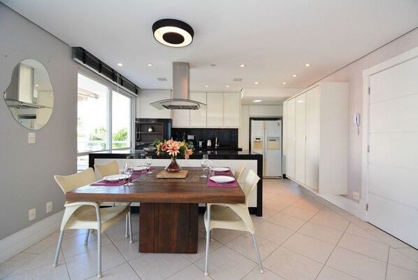 Een moderne keuken met witte kasten, een centraal eiland en een eethoek met een houten tafel en witte stoelen.