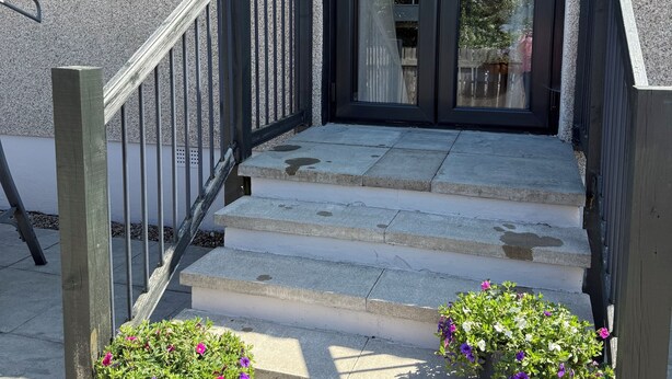 A house with a stone facade, a black door, and a set of concrete steps leading to a wooden door frame.
