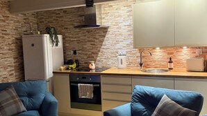 A modern kitchen with a stone backsplash, a built-in oven, and a sink. There are two blue armchairs and a plaid rug on the floor.