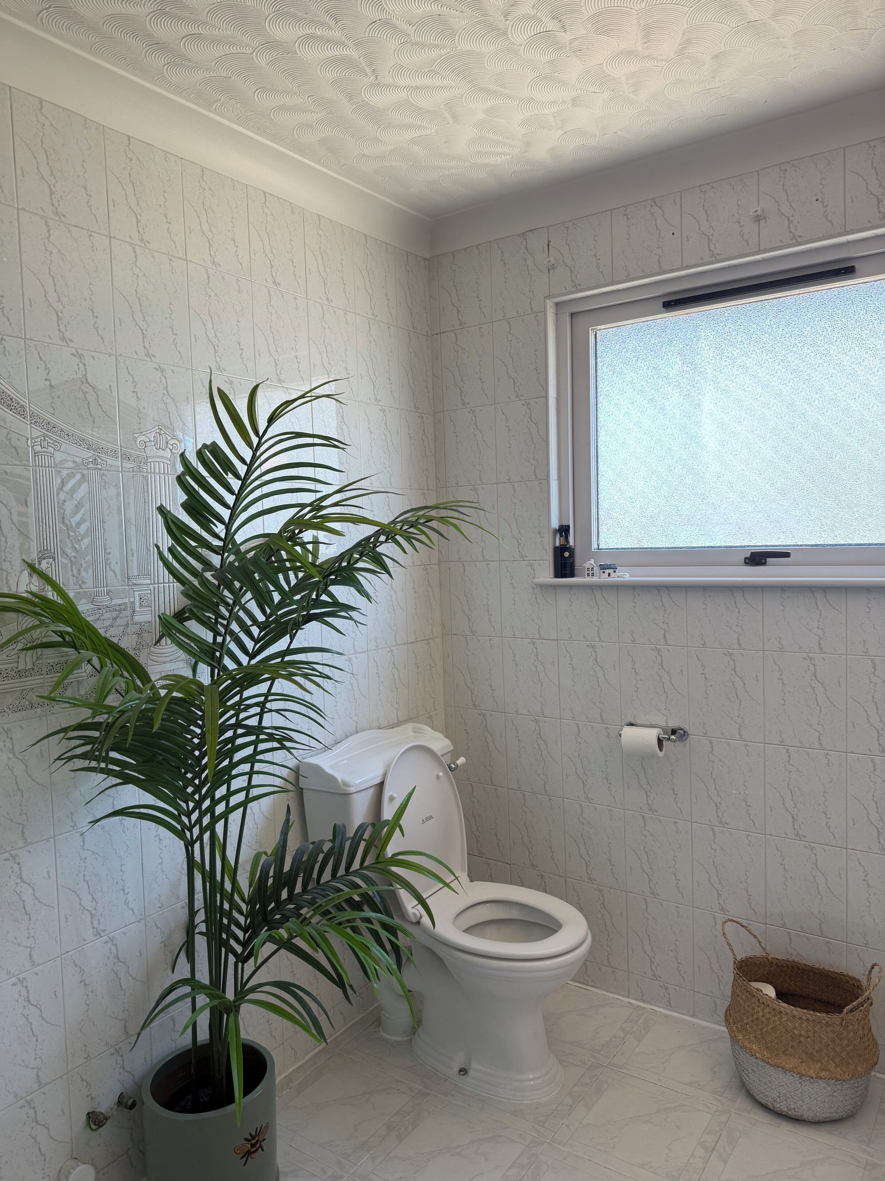 Ein Badezimmer mit Toilette, einem Fenster und einer Topfpflanze.