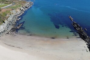 Una playa costera con aguas claras, orilla arenosa y afloramientos rocosos.