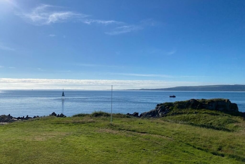 A coastal landscape with a grassy foreground, a lighthouse in the distance, and calm sea.