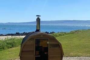 A wooden cabin with a chimney, situated on a grassy area near a body of water.
