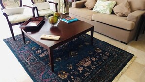 Ein Wohnzimmer mit einer Couch, zwei Sesseln, einem Couchtisch mit einer Obstschale, einem Buch und einer Lampe.