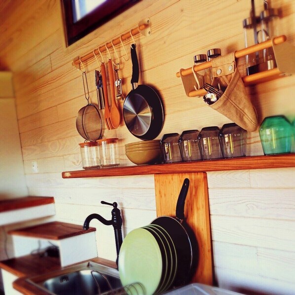 A kitchen with wooden cabinets, a hanging pot rack, and various kitchen utensils. - Tiny house with Nordic bath 10 minutes from the Baie de Somme (Saint-Blimont)