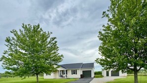 Een gelijkvloers huis met garage, omgeven door een verzorgd gazon en twee grote bomen.