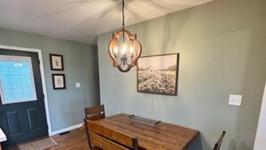 Een eetgedeelte met een houten tafel, stoelen, een kroonluchter en een lijst met een afbeelding aan de muur.