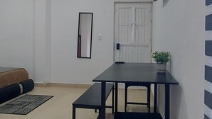 Una habitación con una mesa negra y dos sillas, una planta en maceta, un televisor de pantalla plana montado en la pared, un cuadro enmarco y una puerta con celosía de metal.