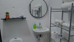 Un baño pequeño y funcional con inodoro, lavamanos y estantería metálica.