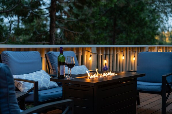 A deck with outdoor seating, a table with a bottle and glass of wine, and string lights. - Whispering Pines Lodge, 25 mi to Yosemite,Baby Friendly, Grill, Game Room (Groveland)