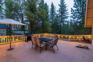 An outdoor patio with a table and chairs, a grill, and string lights.