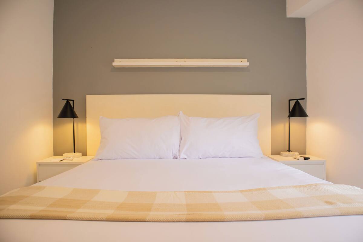 A neatly made bed with white linens, two bedside tables with lamps, and a wall-mounted shelf above the bed.