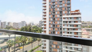 Un edificio de gran altura con varios balcones, vistas despejadas del paisaje urbano circundante y una calle con coches y palmeras abajo.