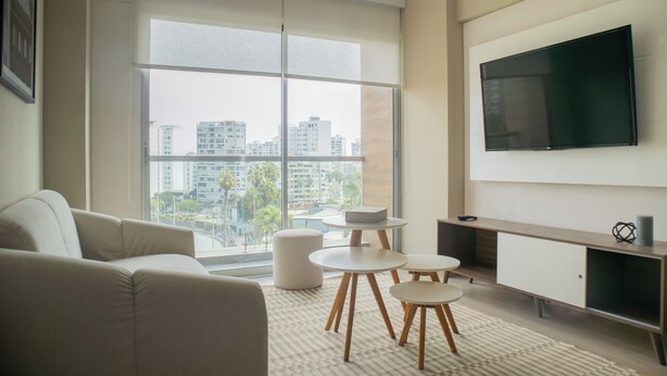 Una sala de estar moderna con un ventanal grande, un televisor de pantalla plana, un sofá y una mesita de centro.