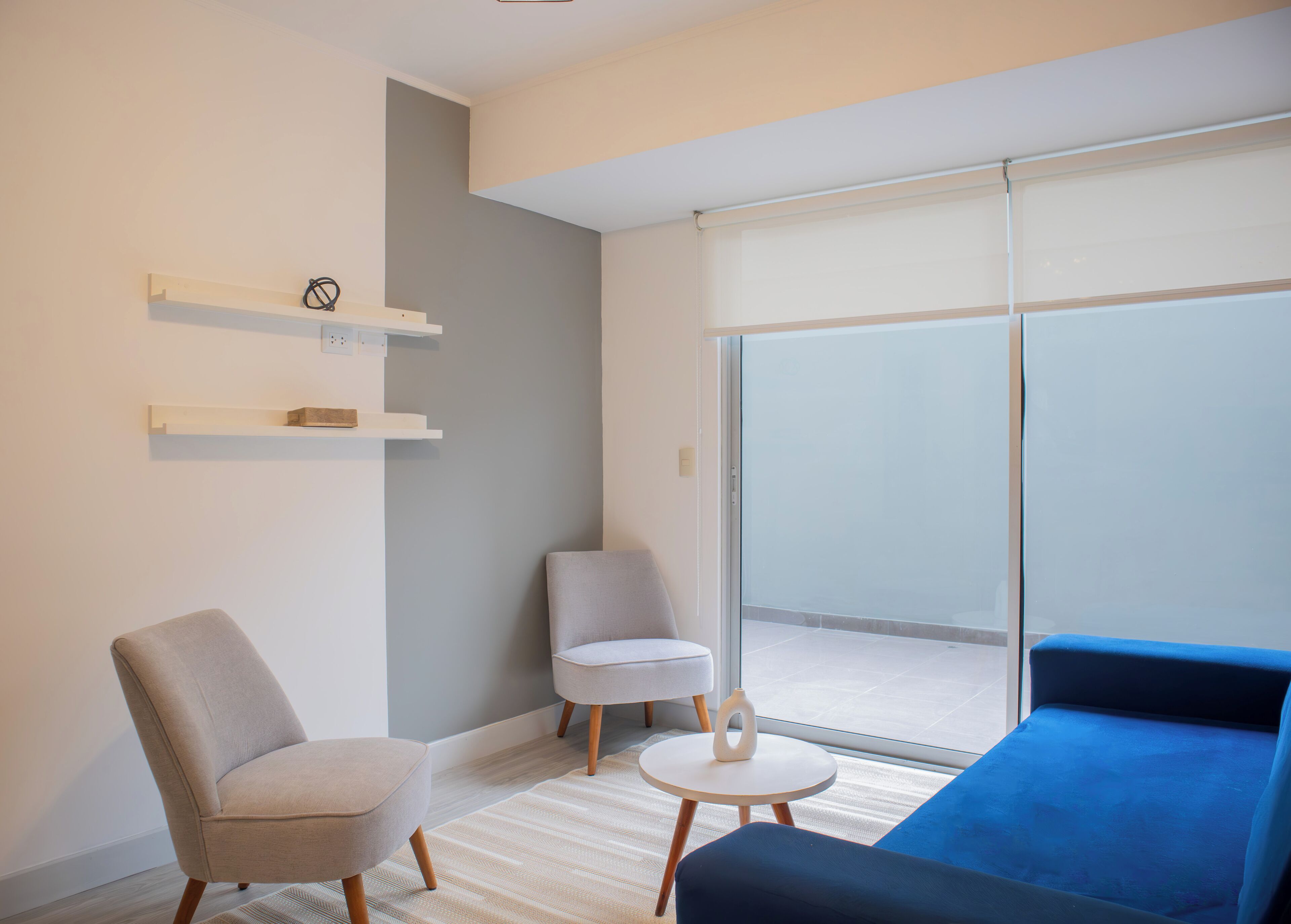 Una sala de estar moderna con un sofá, dos sillones, una mesita y un ventanal corredero a un balcón.