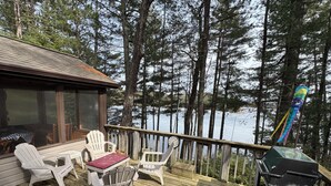 Un pontile in legno con sedie bianche e un barbecue, con vista su un lago circondato da alberi.