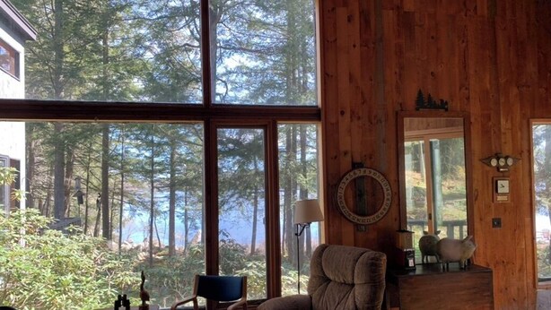A cozy room with large windows, a comfortable armchair, a wooden desk, and a mirror on the wall.